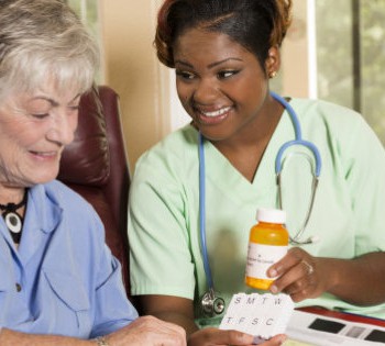Home healthcare nurse with senior adult patient. Medications. Caring, African descent home healthcare nurse conducts medical consultation with senior adult woman at her home or nursing home. The female patient is sitting in her comfortable chair while reviewing her medications information with her nurse or doctor. Backyard can be seen through the windows.